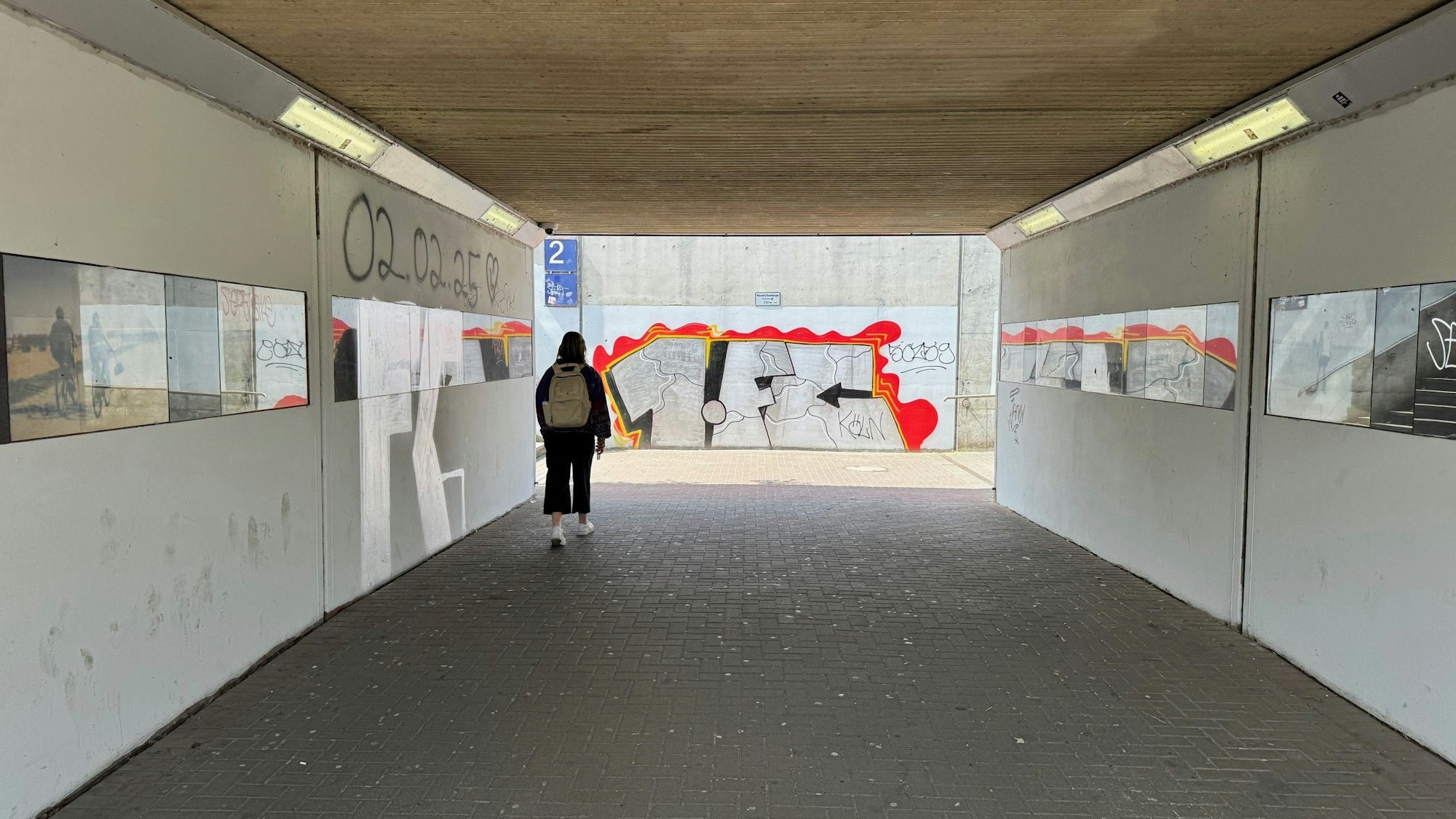 Eine Unterführung, rechts und links Bilder, im Hintergrund eine gesprayte Ziffer und Buchstaben.