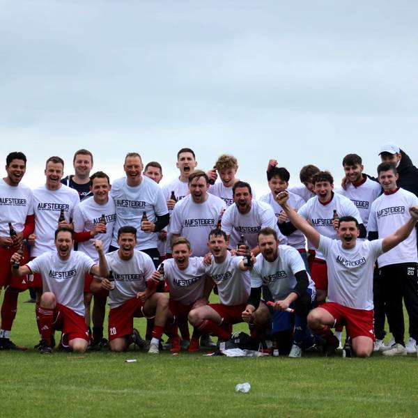Das Foto zeigt eine Fußball-Mannschaft in weißen Trikots und roten Hosen, die für ein Foto posiert.