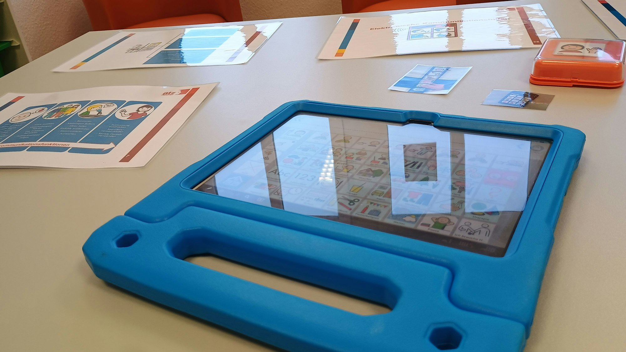 Das Bild zeigt den Talker, ein blaues Tablet, das verschiedene Bilder als Kacheln zeigt, mit denen anhand von Symbolen kommuniziert werden kann.