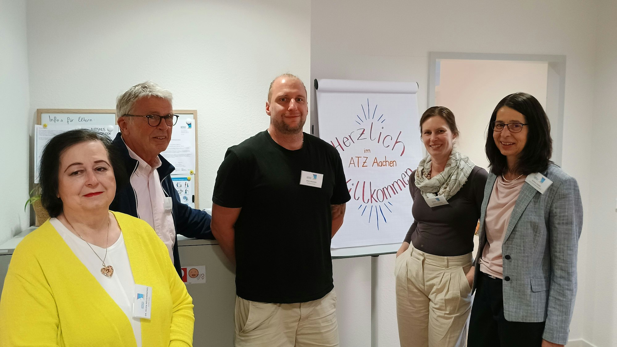 Das Bild zeigt fünf Menschen, in der Mitte zudem ein großer Zettel mit der Aufschrift: Herzlich Willkommen im ATZ Aachen.