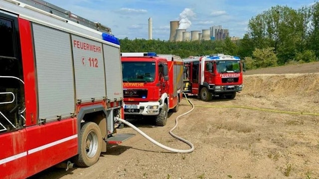 Drei Einsatzwagen stehen auf dem Gelände, im Hintergrund das Kraftwerk Niederaußem.