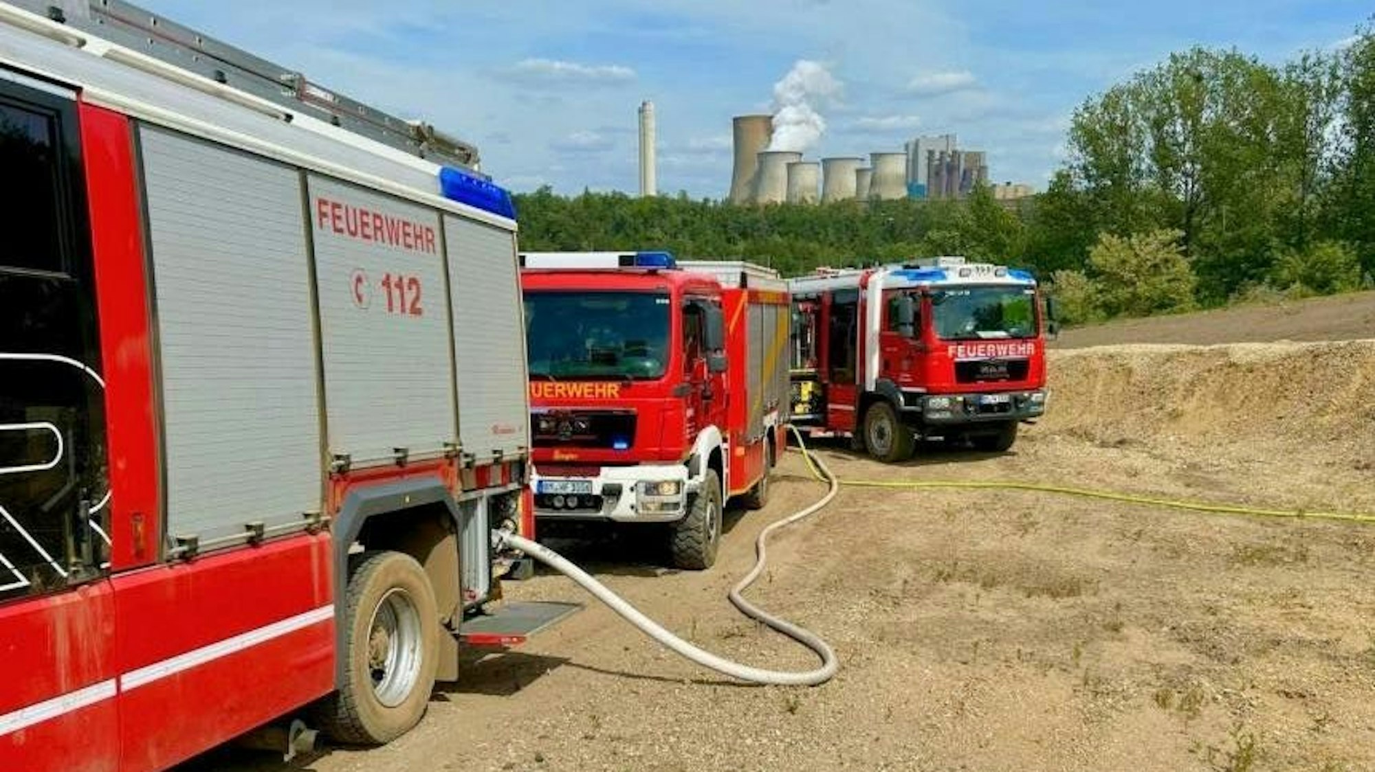 Drei Einsatzwagen stehen auf dem Gelände, im Hintergrund das Kraftwerk Niederaußem.