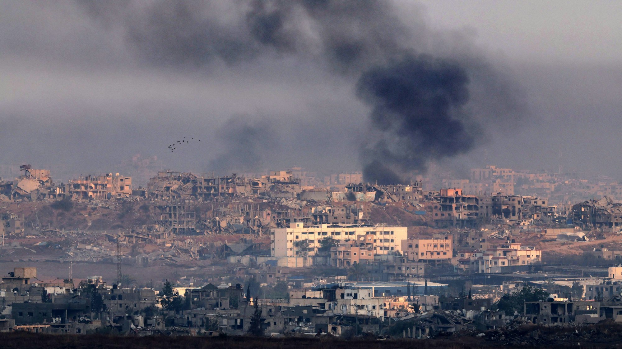 Rauch über zerstörten Gebäuden im Gazastreifen: Israel bombardiert erneut das Küstengebiet – rund 90 UN-Hilfstransporte sind unterwegs.