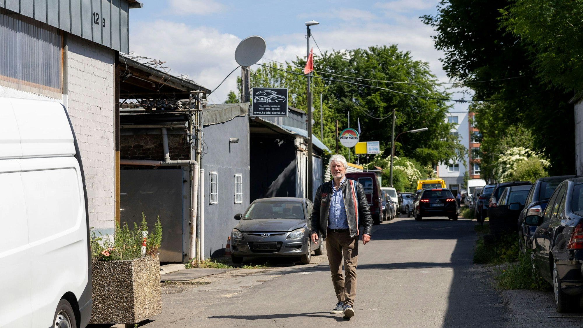Ein Mann geht auf einer Straße, an denen Autos geparkt sind und einige Schilder am Rand auf Betriebe schließen lassen.