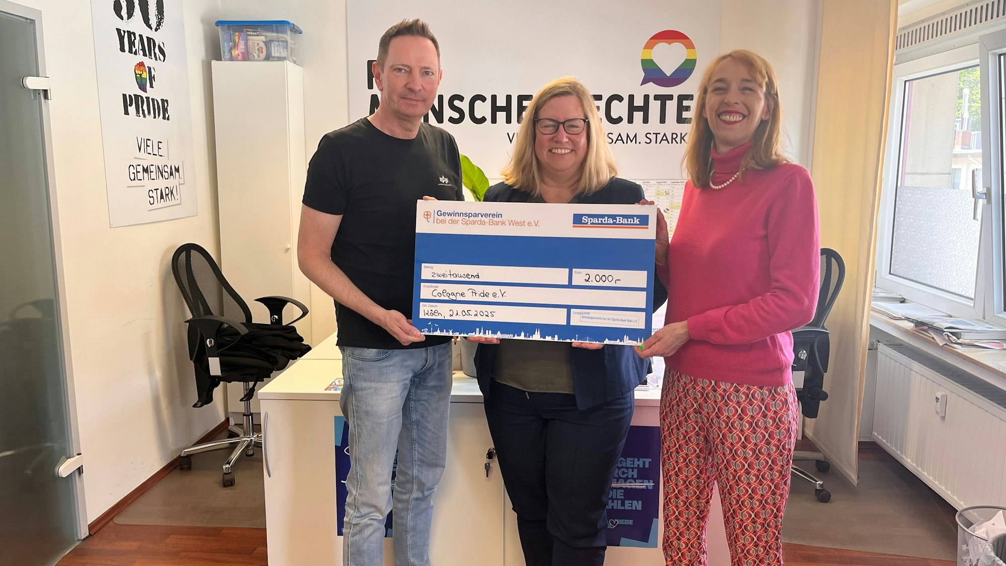 Tanja Decking (m.) Generalbevollmächtigte der Sparda Bank West überreicht Natalie Hagen (r.) und Uwe Weiler (l.) vom Cologne Pride e.V. den Scheck über 2000 Euro im Büro der Vereins.