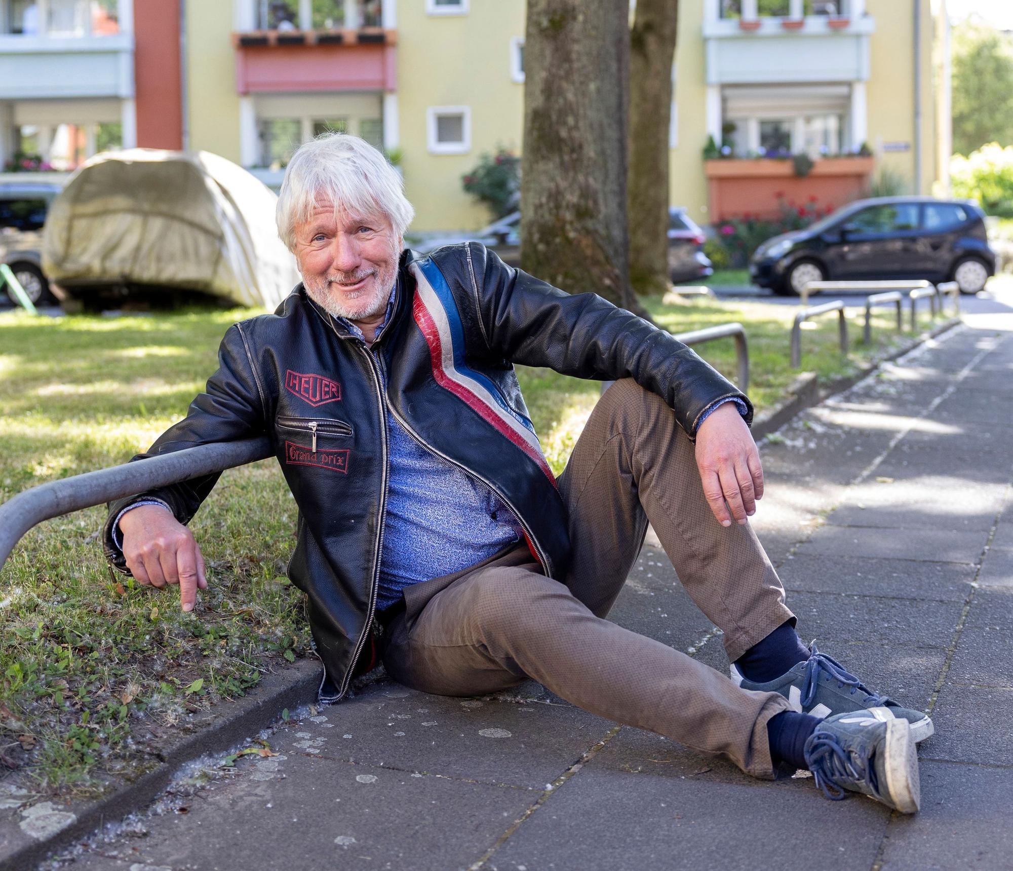 Ein Mann sitzt auf dem Bürgersteig am Rande einer von Metall-Absperrungen begrenzten Grünfläche.