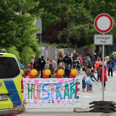 Zu sehen ist ein Banner mit der Aufschrift „Schulstraße“ und dahinter spielende Kinder.
