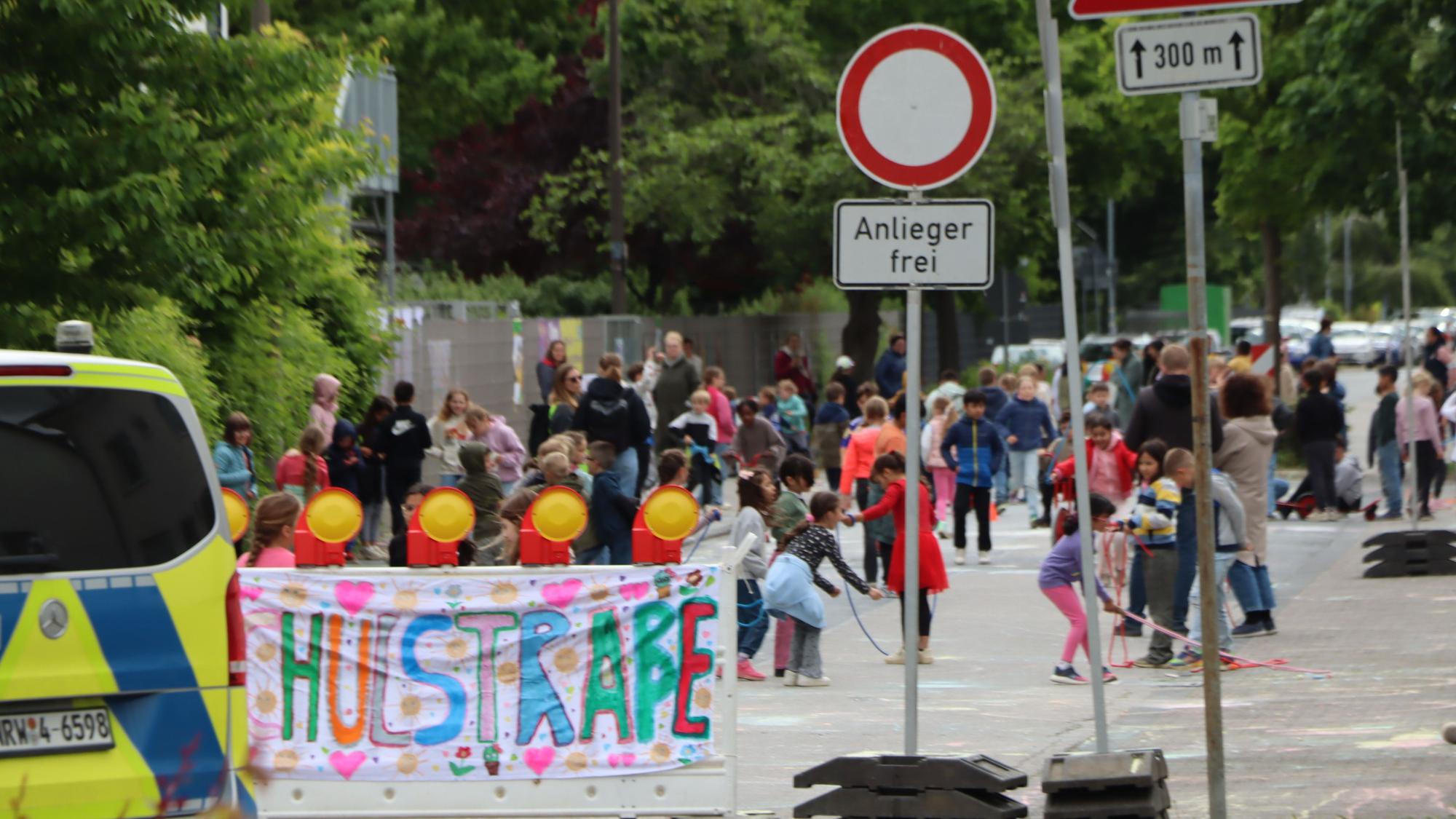 Zu sehen ist ein Banner mit der Aufschrift „Schulstraße“ und dahinter spielende Kinder.