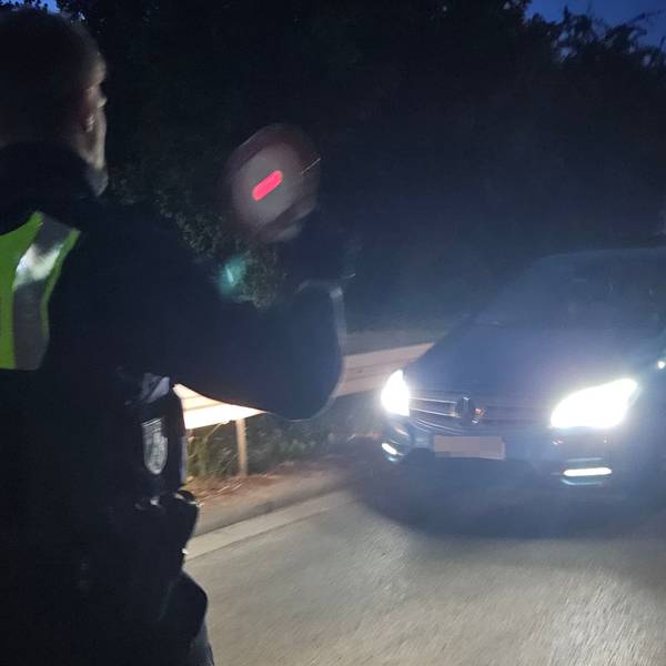 Ein Polizist winkt mit einer roten Kelle ein Fahrzeug aus dem Verkehr.