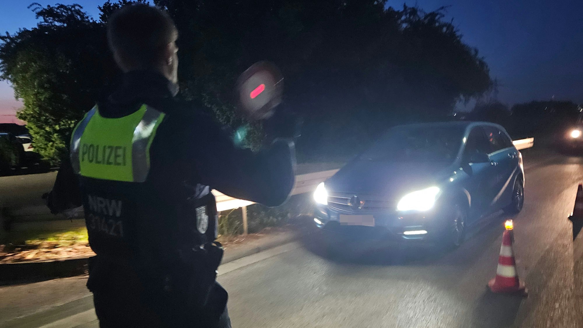 Ein Polizist winkt mit einer roten Kelle ein Fahrzeug aus dem Verkehr.