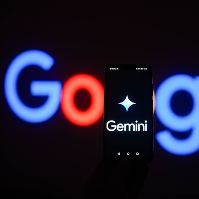 Ein Smartphone, auf dessen Bildschirm ein Gemini-Logo zu sehen ist, steht vor einem leuchtenden Google-Logo