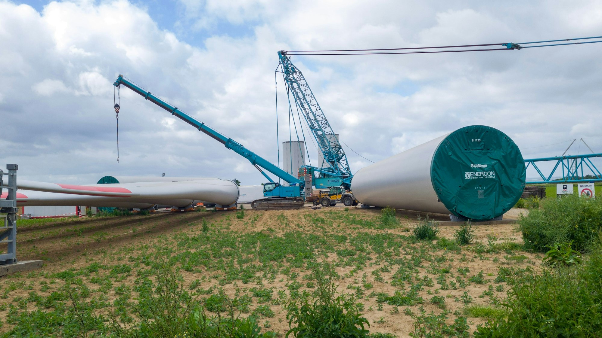 Die einzelnen Bauteile eines Windrades liegen um einen blauen Kran herum auf einem Feld bei Zülpich-Rövenich.