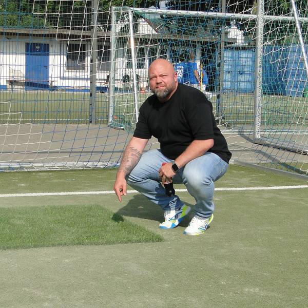 Ein Mann zeigt auf neuen und alten Kunstrasen auf einem Kunstrasen-Fußballplatz.
