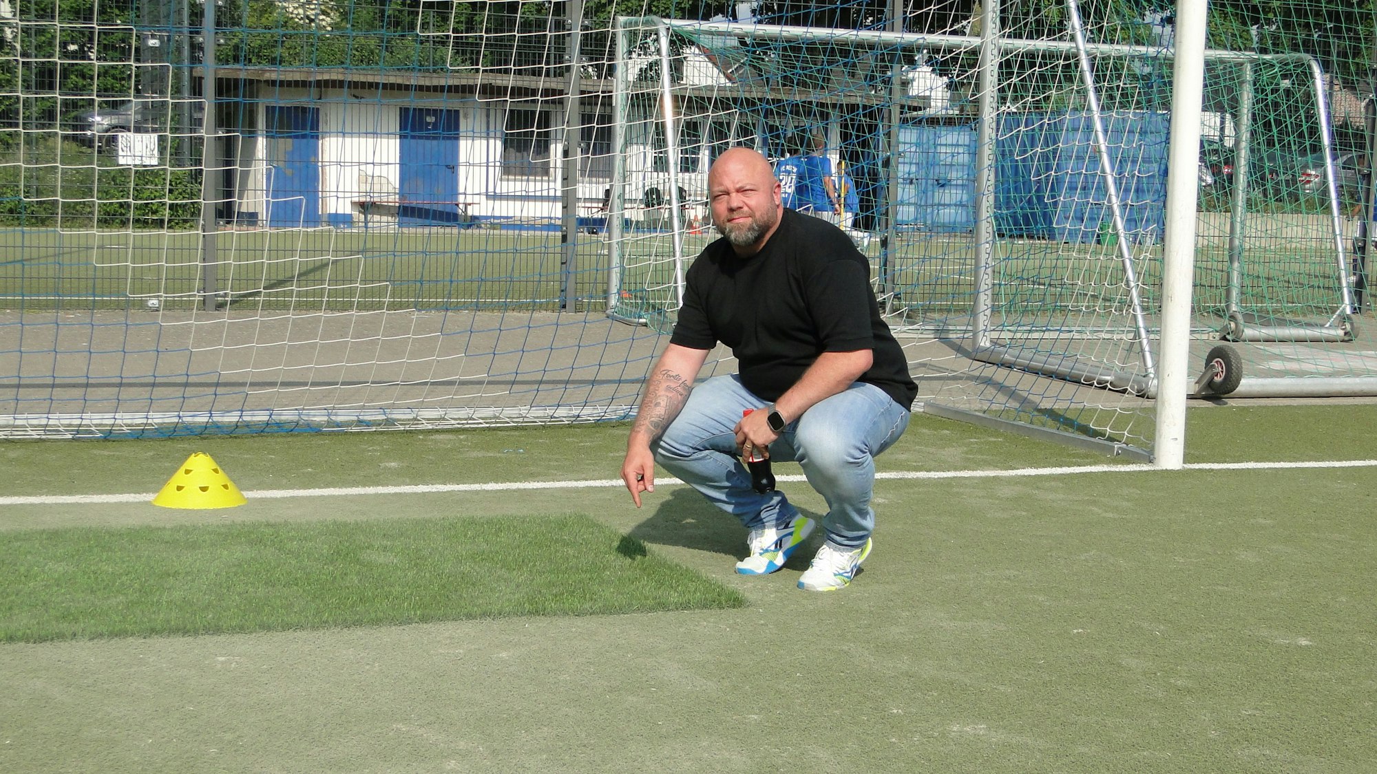Ein Mann zeigt auf neuen und alten Kunstrasen auf einem Kunstrasen-Fußballplatz.
