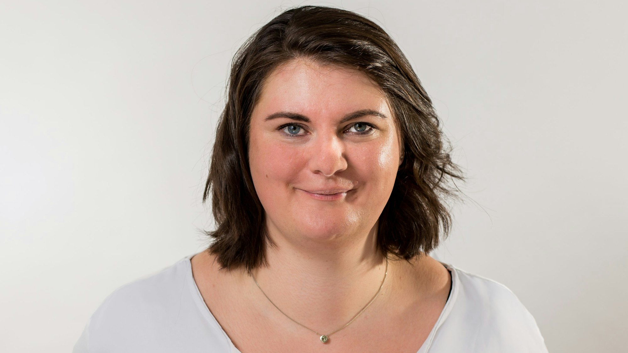 Auf dem Foto ist eine junge Frau mit dunklem Haar zu sehen, das ihr bis zu den Schultern reicht. Sie trägt eine goldene Halskette.