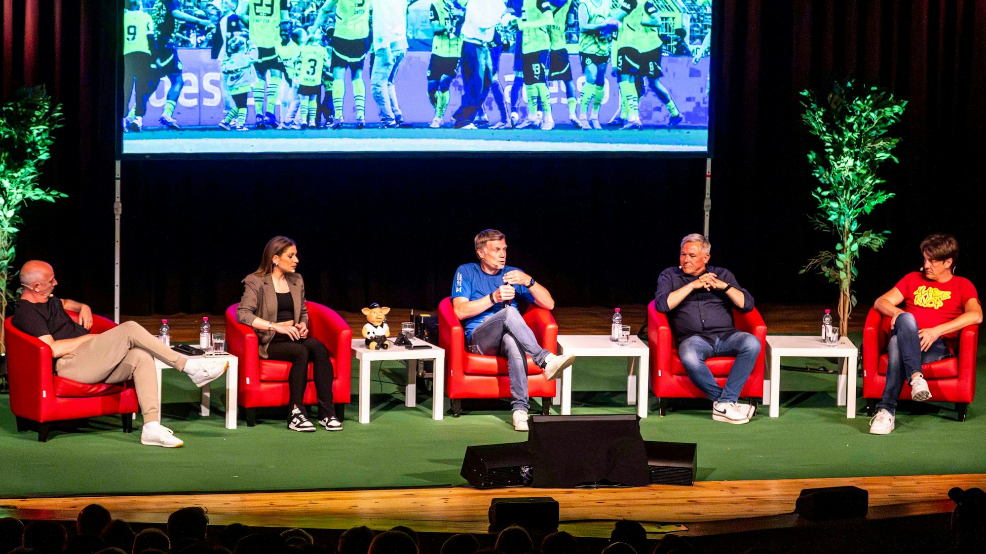 Das Bild zeigt die Fußballexperten auf der Bühne im Stadttheater. Sie sitzen in roten Sesseln.