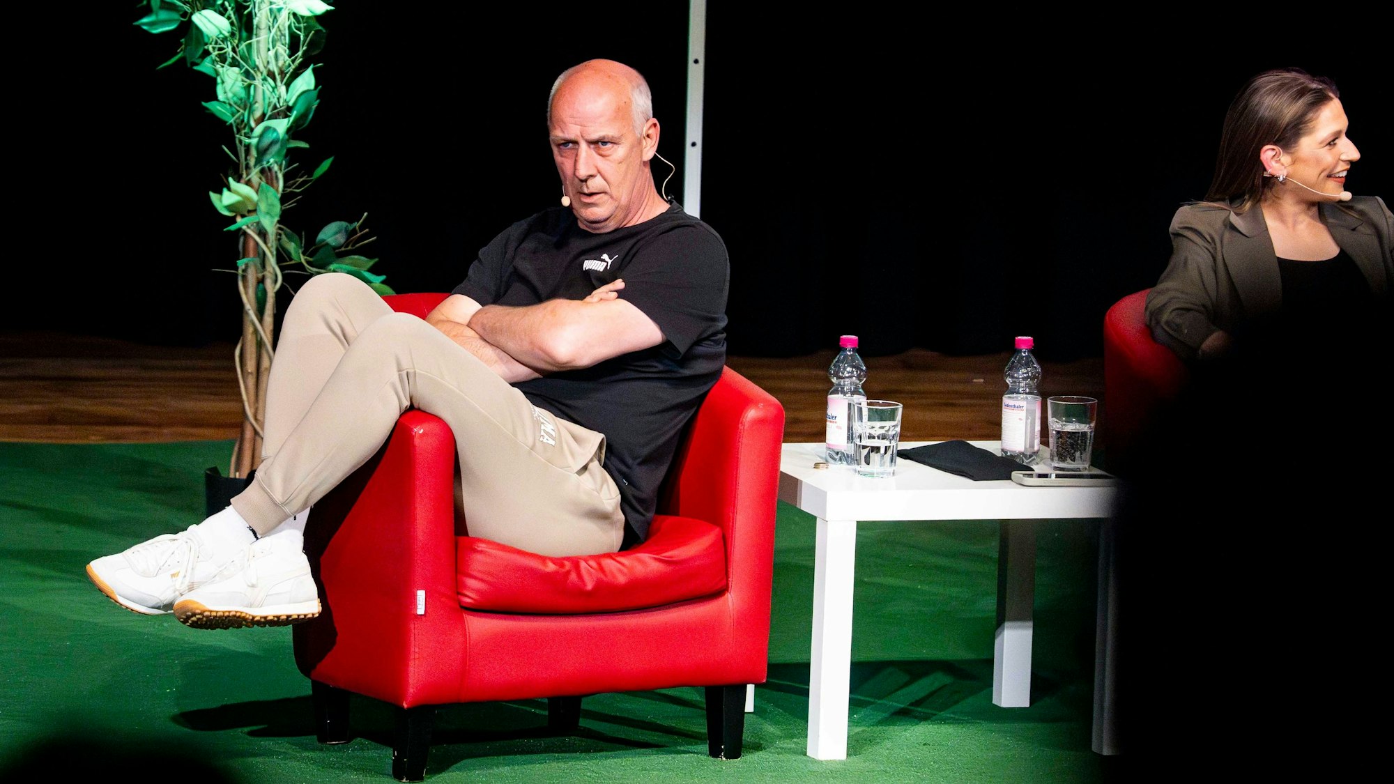 Das Bild zeigt Mario Basler, der in einem roten Sessel mit verschränkten Armen sitzt.