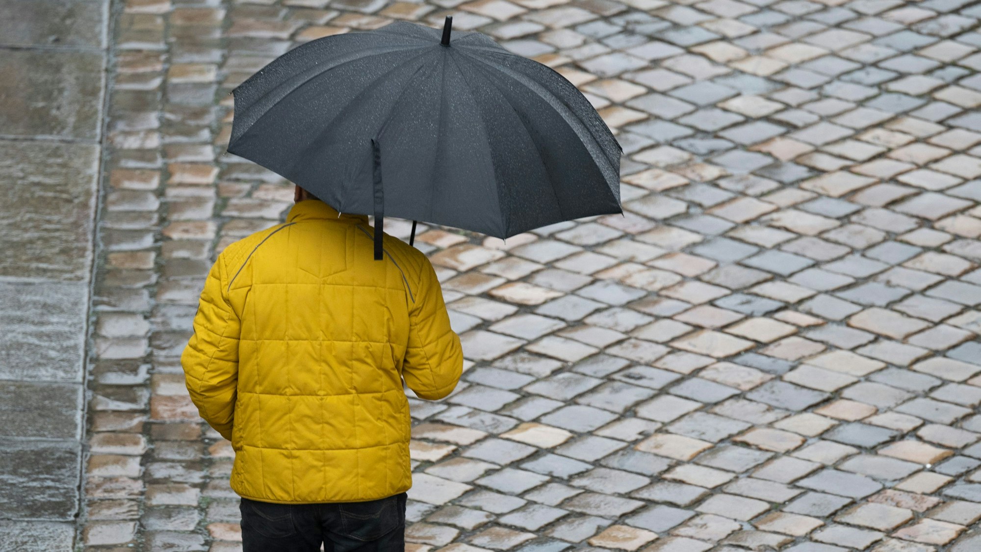 Ein Passant mit einem Regenschirm geht auf einer gepflasterten Straße entlang. Laut Vorhersage soll das Wetter zum Monatsende regnerisch werden.