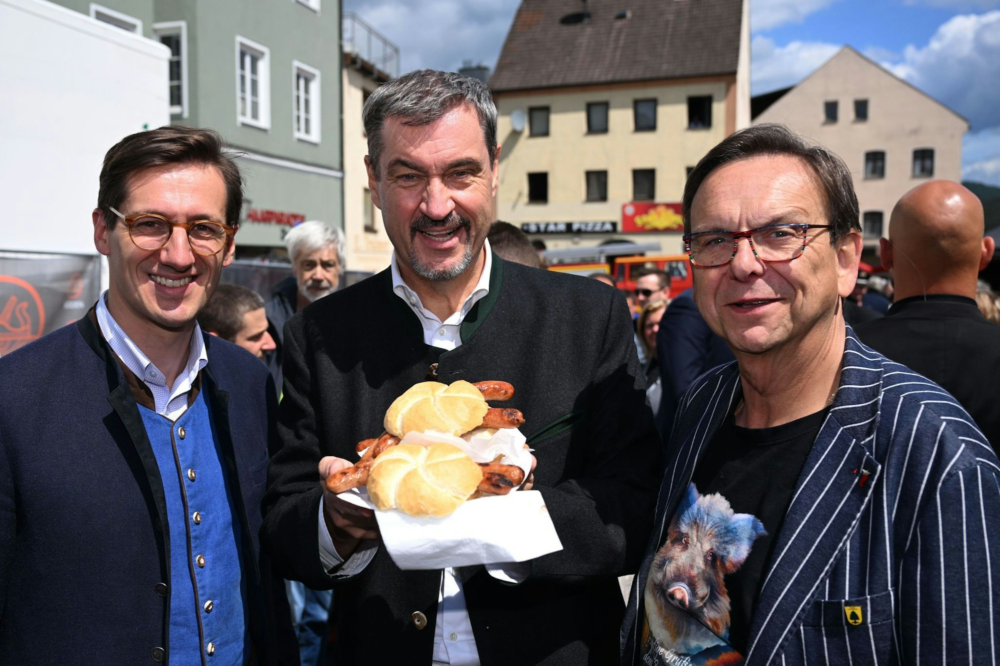 Markus Söder (M.) hält Bratwurst-Semmeln in die Kamera.