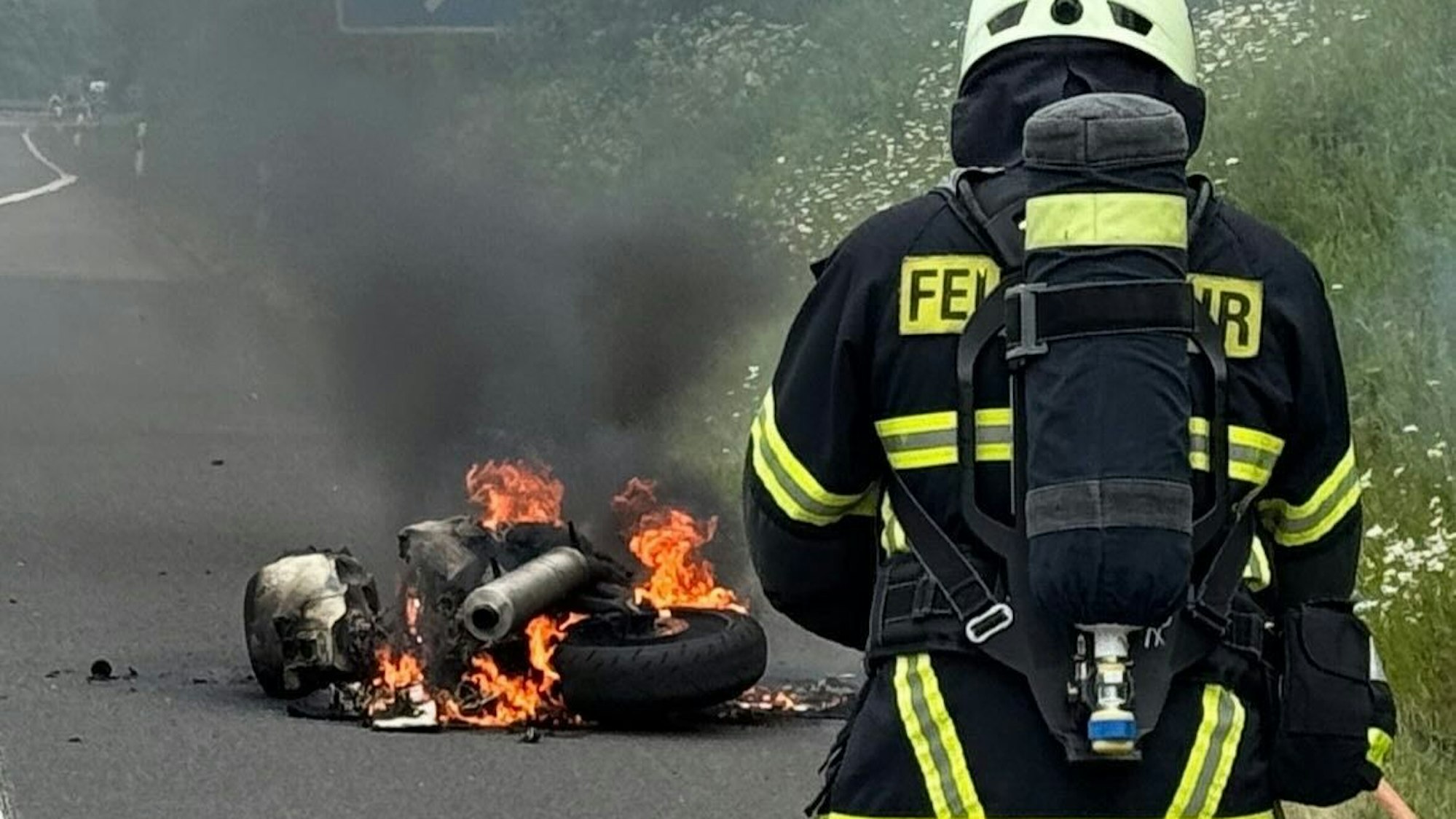 Ein Feuerwehrmann steht in mehreren Metern Entfernung vor einem brennenden Motorrad.