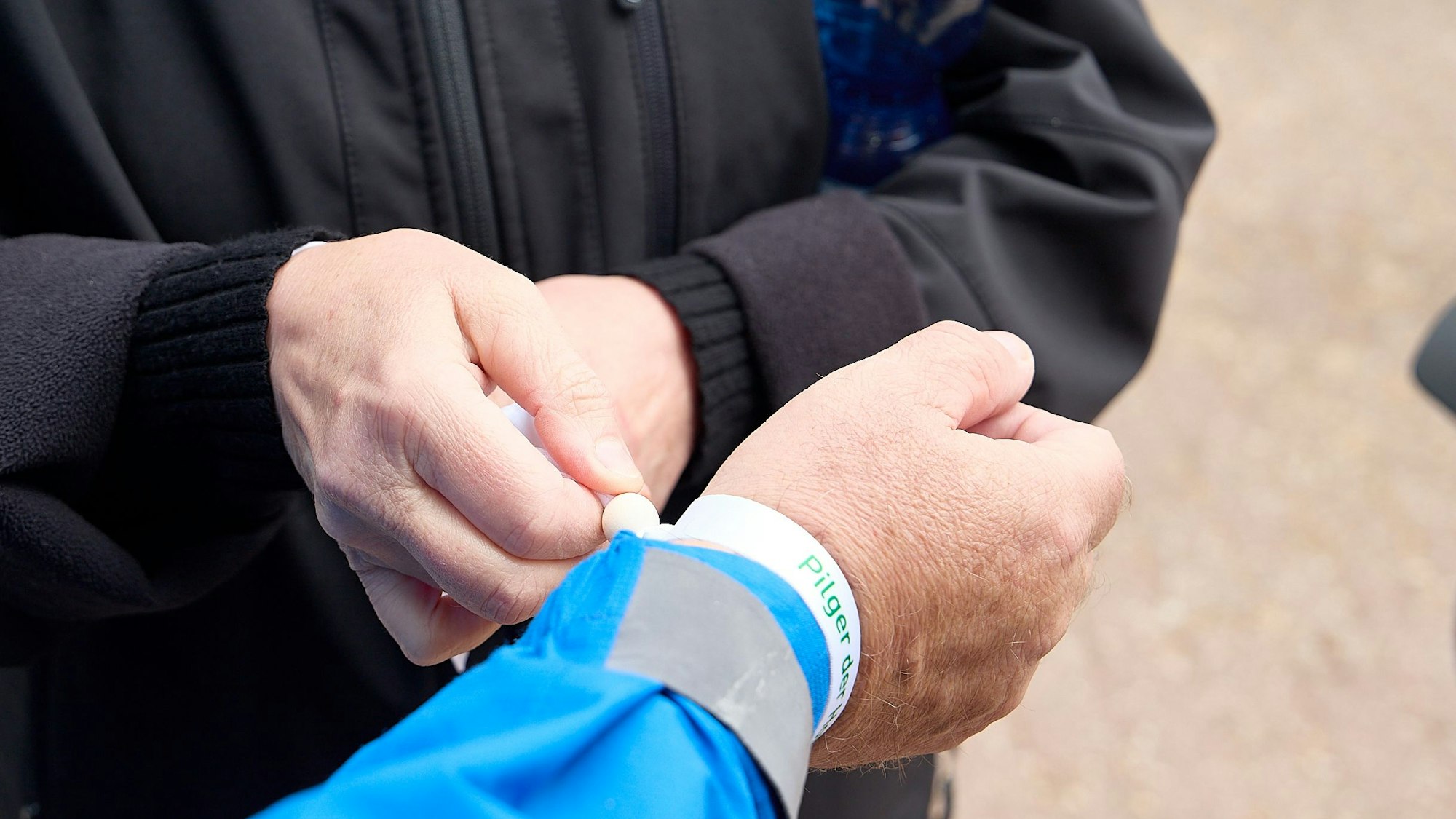 Man sieht, wie einem Pilger ein Band am Handgelenk befestigt wird.