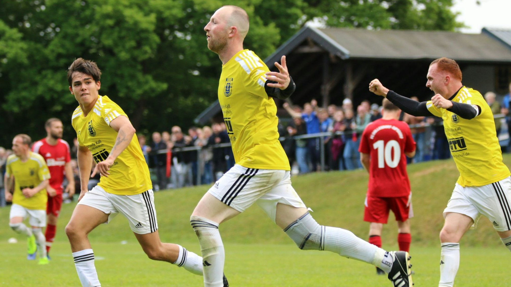Ein Fußballer läuft mit ausgestreckten Armen nach einem Treffer über den Platz. Auch seine Mitspieer jubeln.