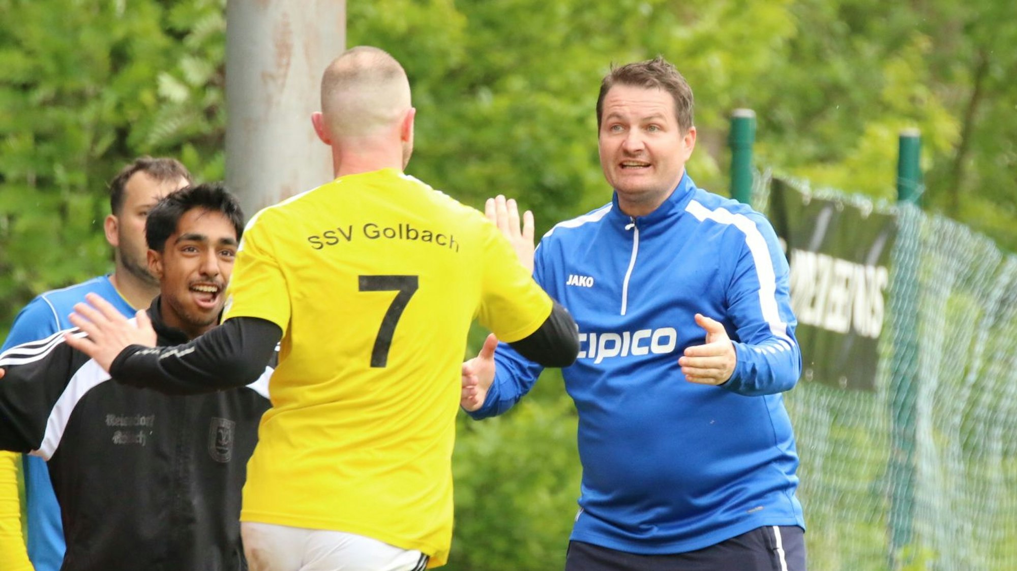 Ein Co-Trainer macht sich zum Jubeln mit einem Torschützen bereit, der auf ihn zuläuft.