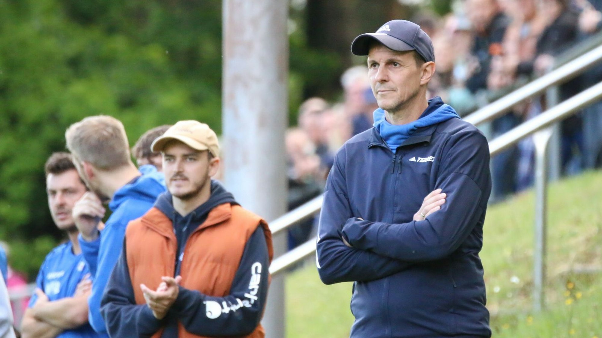Der Co-Trainer der Verlierermannschaft hat die Arme vor der Brust verschränkt.