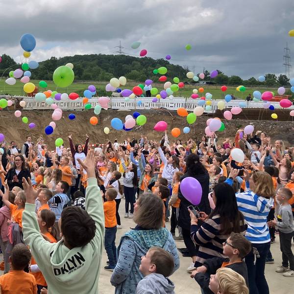 Schülerinnen und Schüler sowie Lehrkräfte lassen bunte Luftballons steigen.