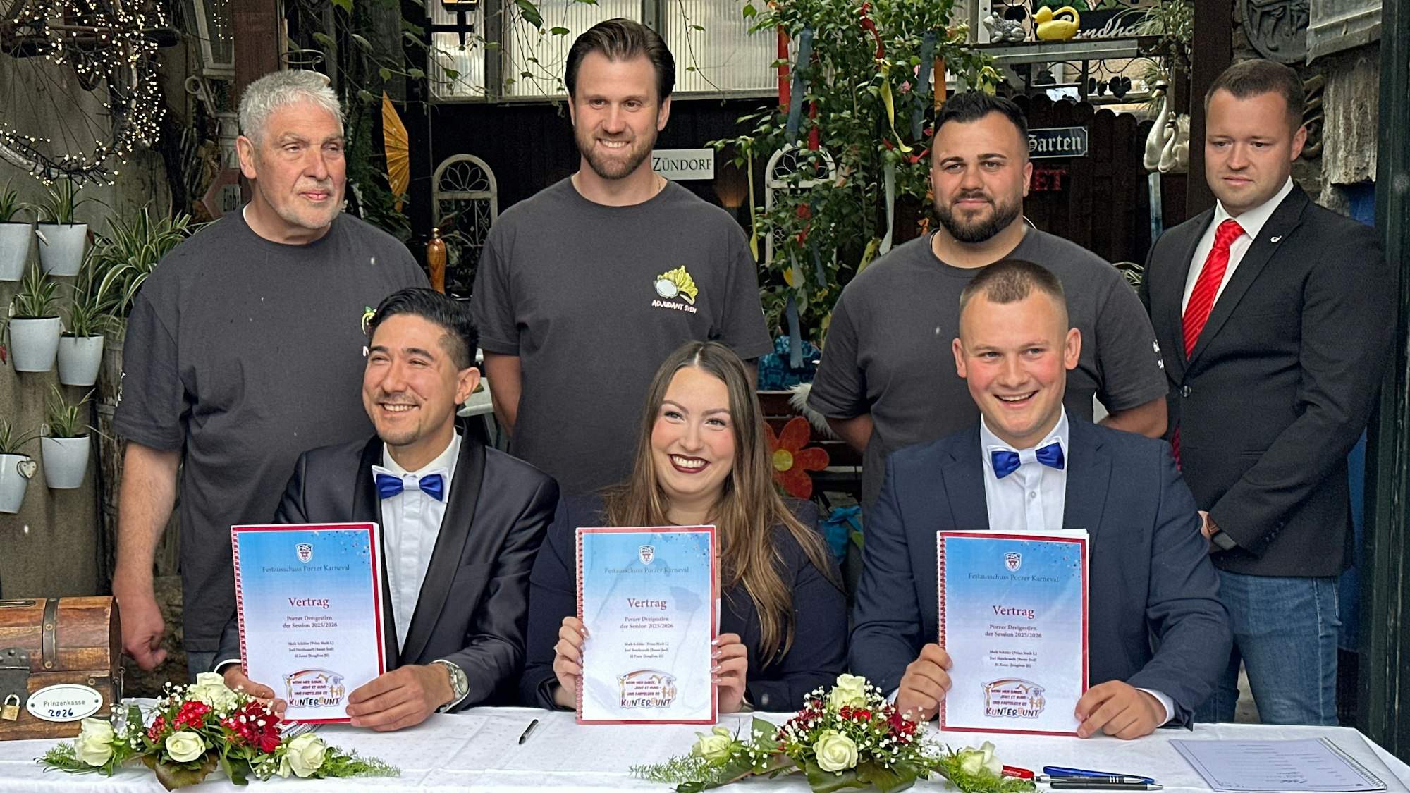 Das künftige Porzer Dreigestirn 2026 mit seinen Adjutanten hält die frisch unterschriebenen Verträge hoch: Prinz Maik I., Jungfrau Jil und Bauer Joel (v.r.).