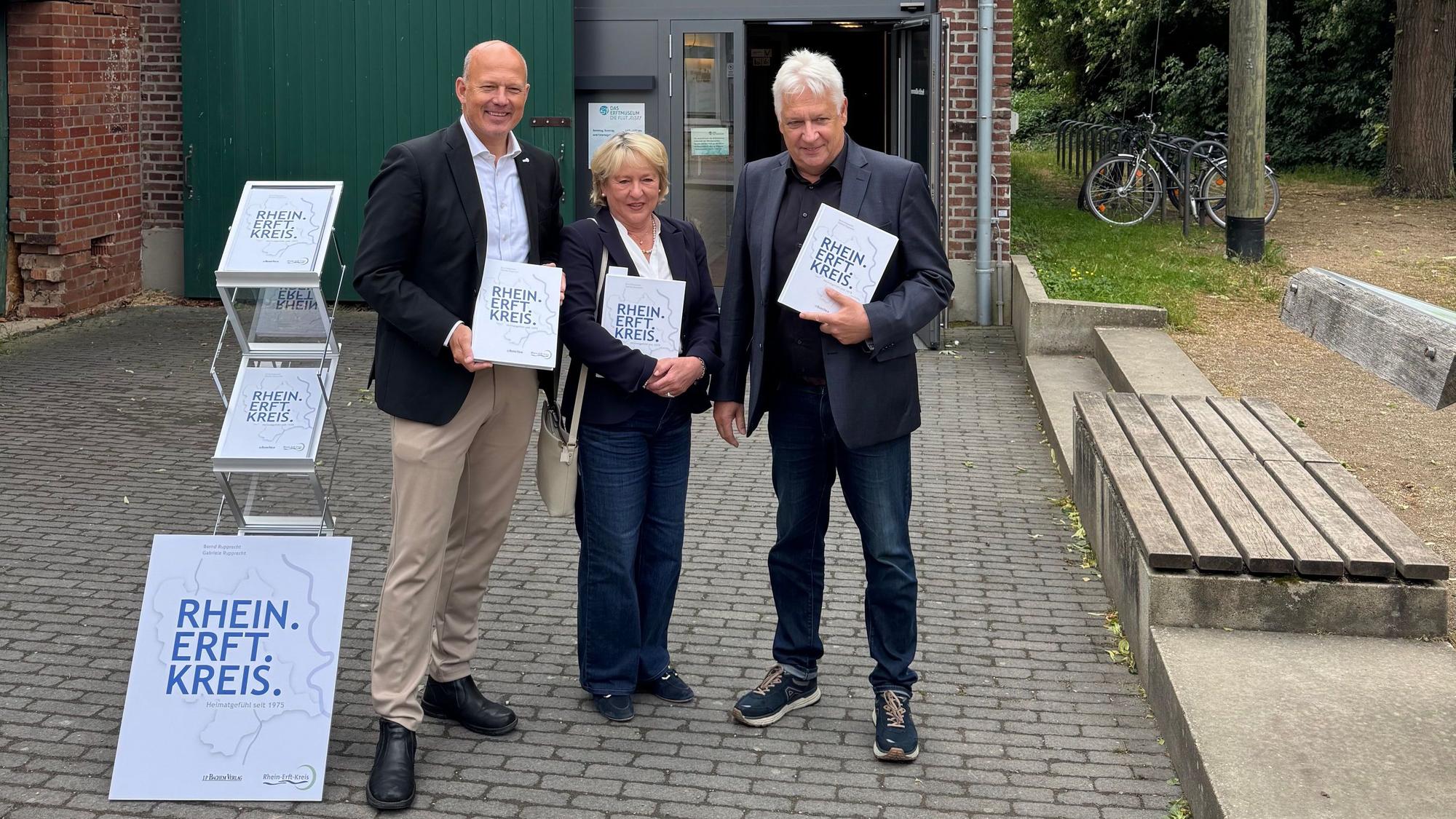 Eine Frau und zwei Männer halten jeweils ein Buch.