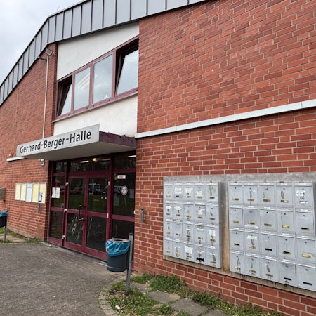 Auf dem Bild ist eine Turnhalle zu sehen. Neben dem Eingang sind Briefkästen für die dort untergebrachten Menschen montiert.