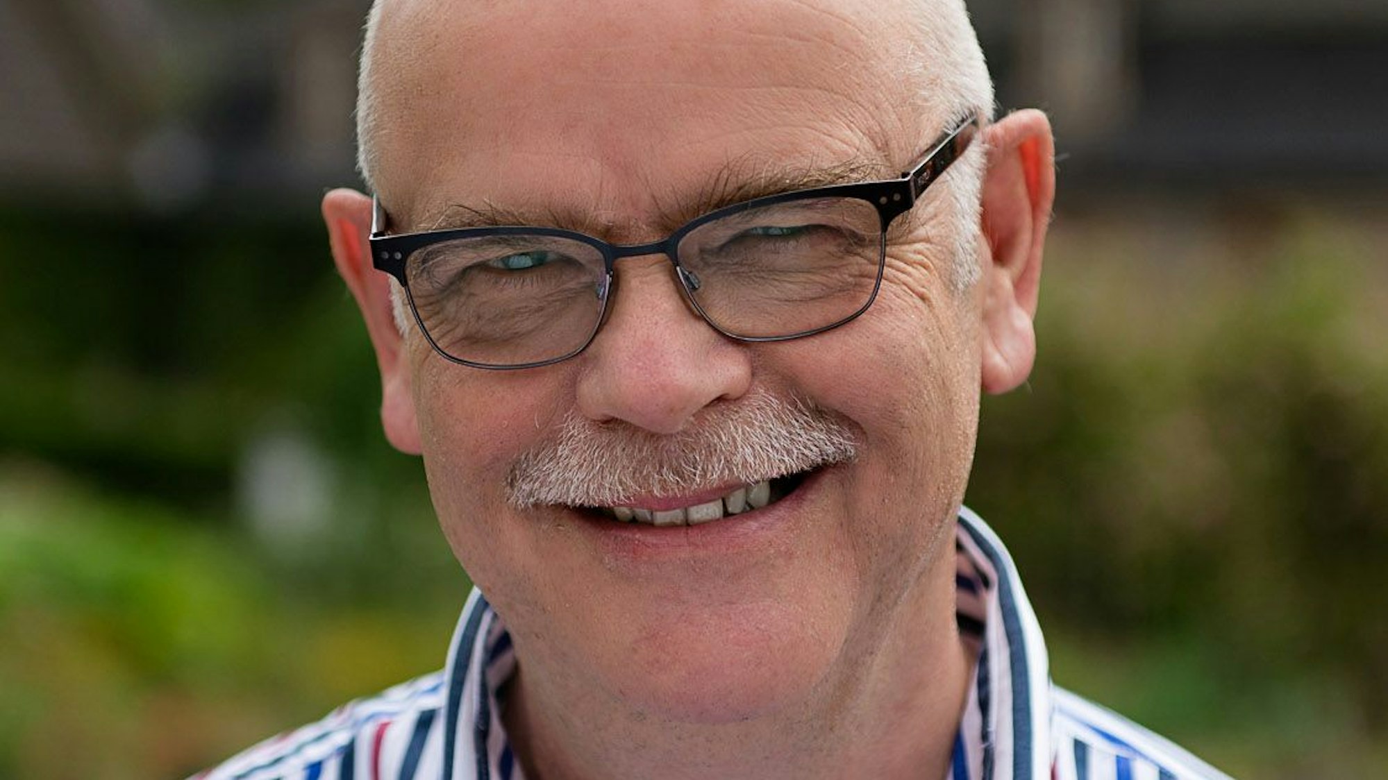 Auf dem Foto ist ein Mann mit grauem Schnauzbart und Brille zu sehen.
