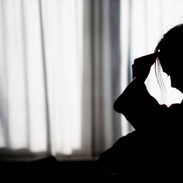 Die Silhouette einer Frau zeichnet sich vor einer hellen Fensterfront ab.