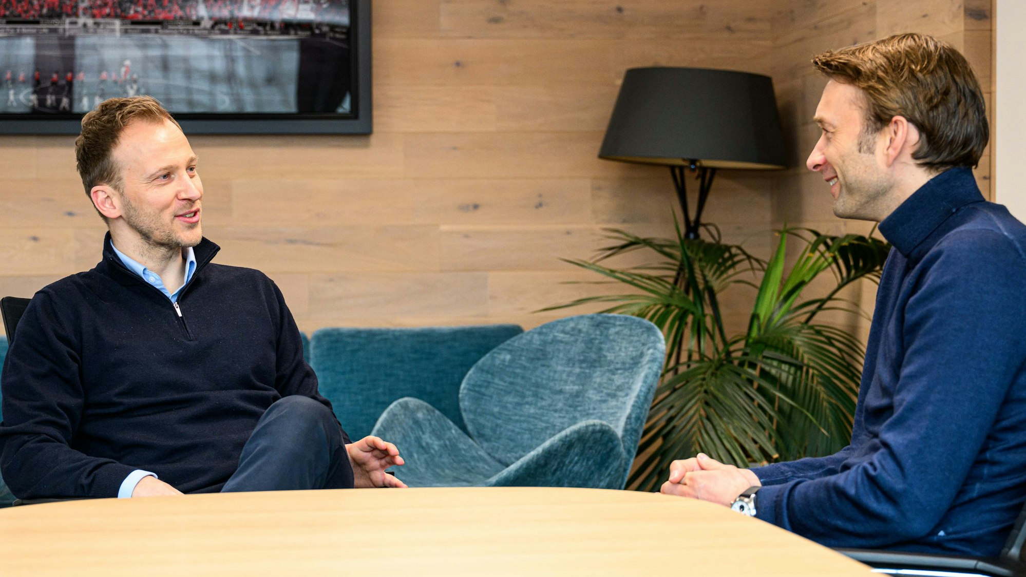 Zwei ehemalige Fußballprofis sitzen an einem Tisch zusammen und besprechen sich.