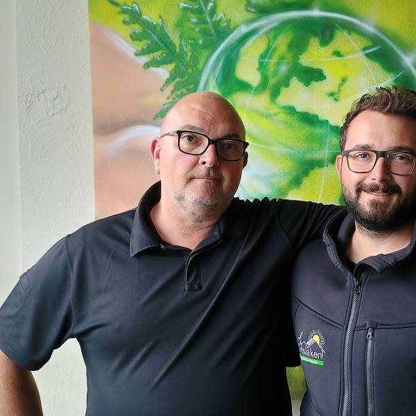 Oliver Dinslaken hat den Arm um seinen Sohn Max gelegt. Hinter ihnen ist ein Graffito, das einen grünen Globus und die Kölner Hohenzollernbrücke zeigt.