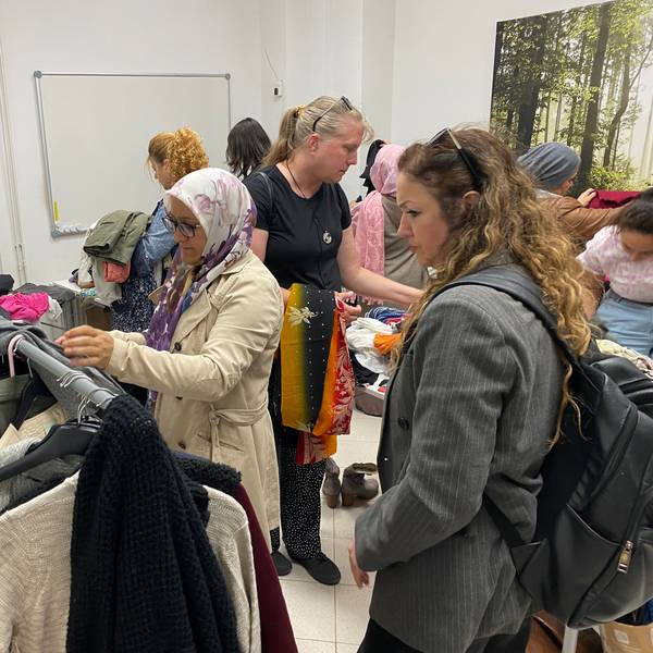 Mehrere Frauen sehen sich Kleidung an, die auf Tischen liegt oder an Ständern hängt.