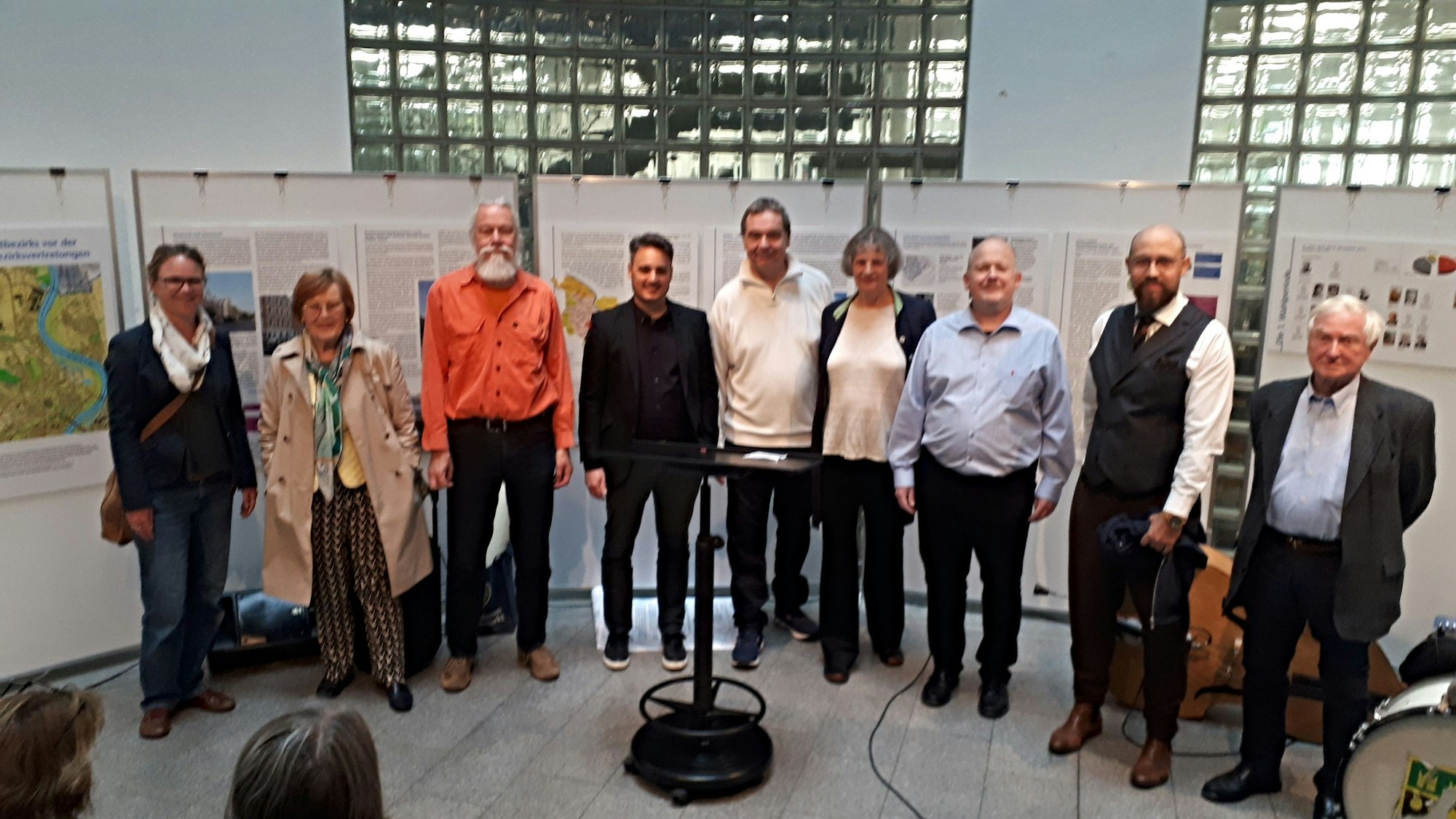 Neun Menschen stehen im Halbrund vor Aufstellwänden, die die Geschichte der Bezirksvertretung dokumentieren.
