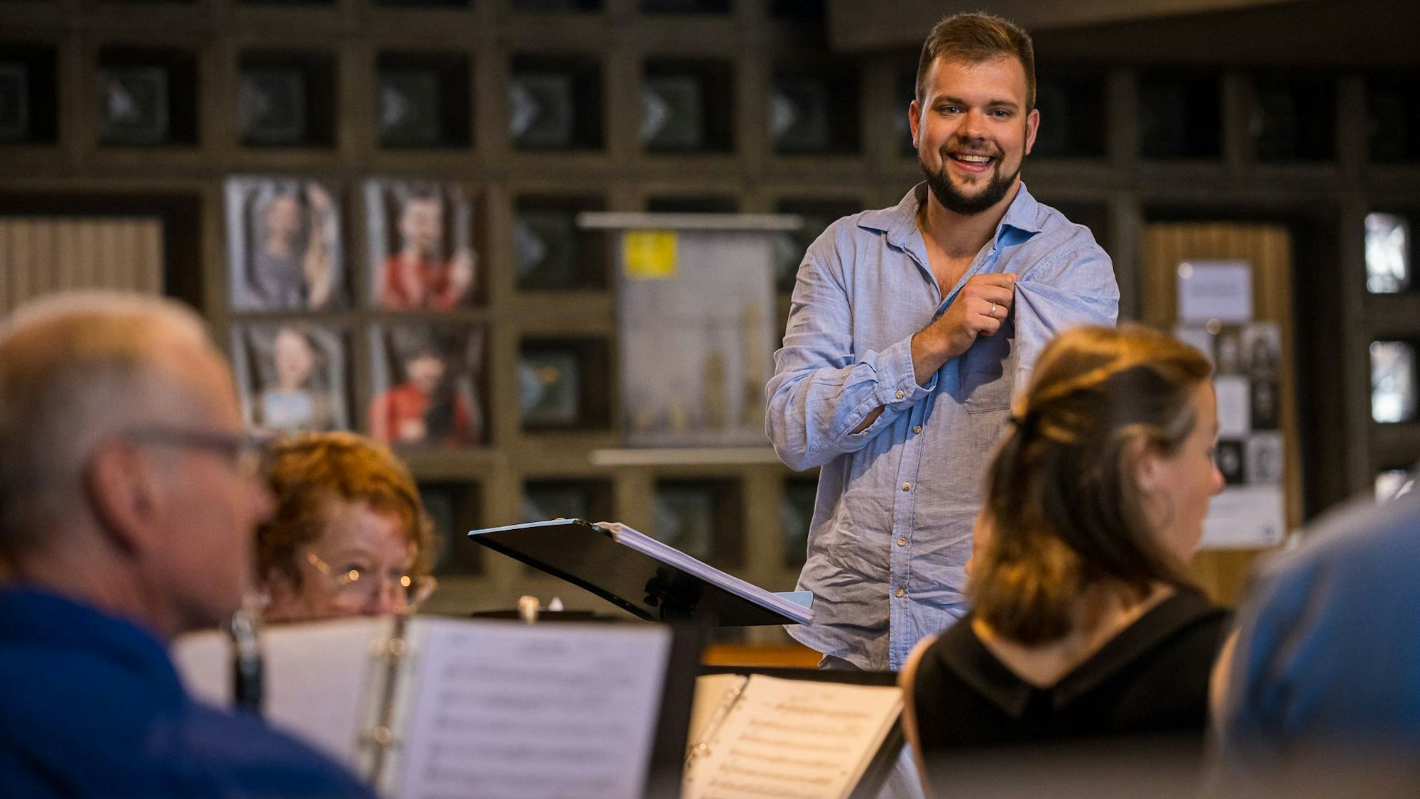 Ein junger Mann steht lachend an einem erhöhten Platz. Vor ihm sitzen Musiker.
