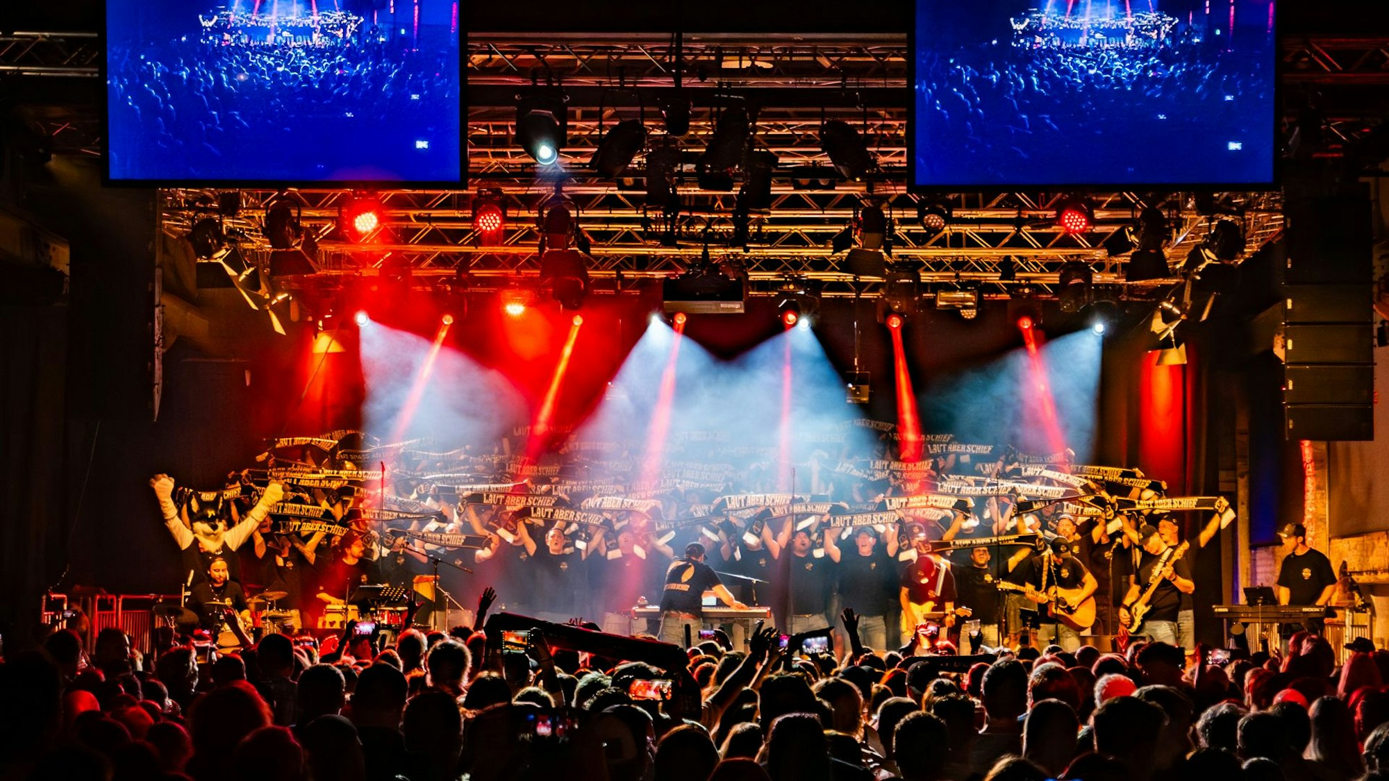 In der Halle 32 in Gummersbach steht ein Chor auf der Bühne, der Schals in die Höhe hält.