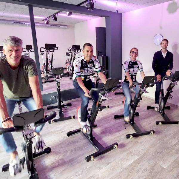 Drei Männer und eine Frau sitzen auf Cycling-Rädern und lachen in die Kamera.