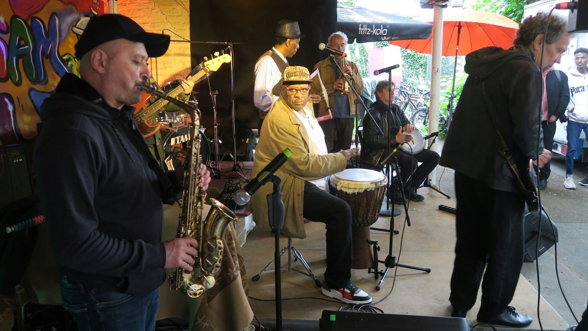 Verschiedene Musiker stehen auf einer niedrigen Bühne.