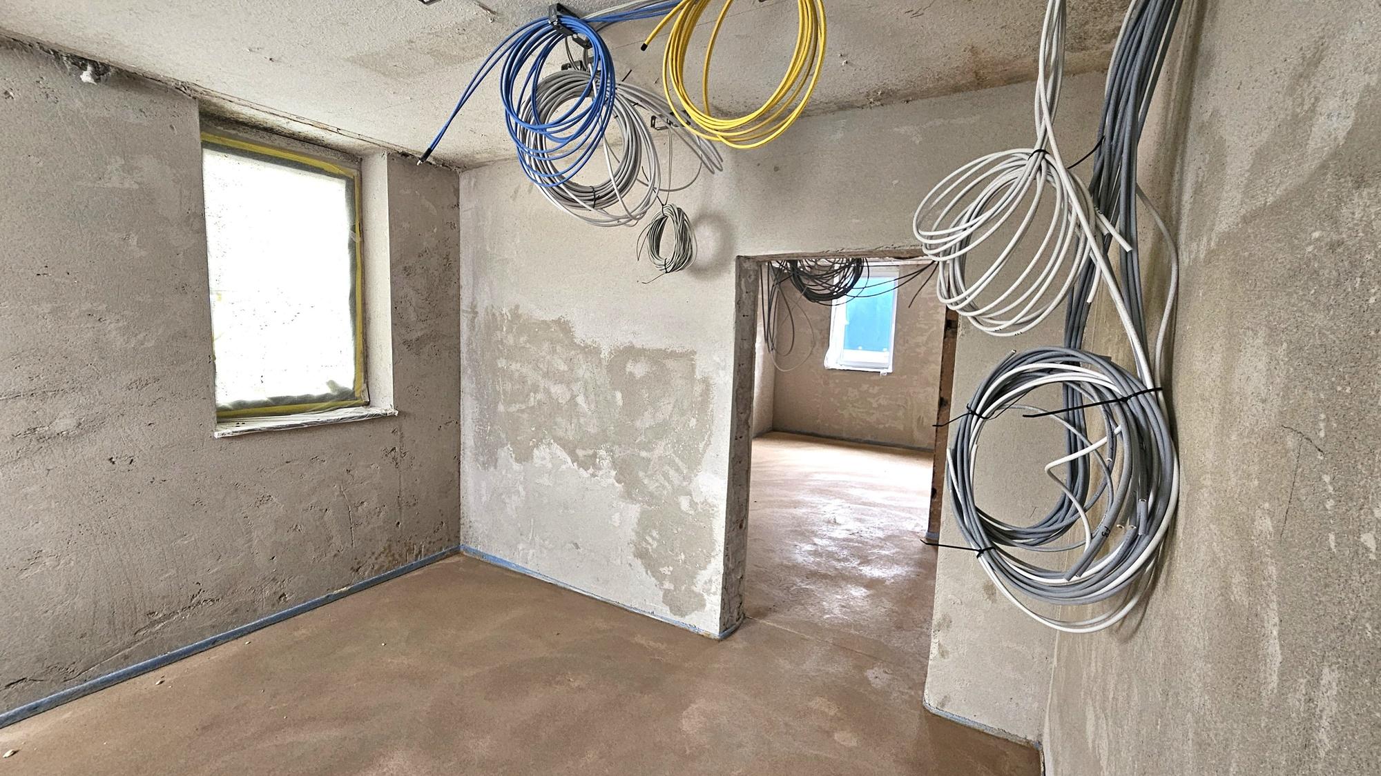Blick in Räume mit neu verputzten Wänden. Von der Decke hängen Kabel in verschiedenen Farben.