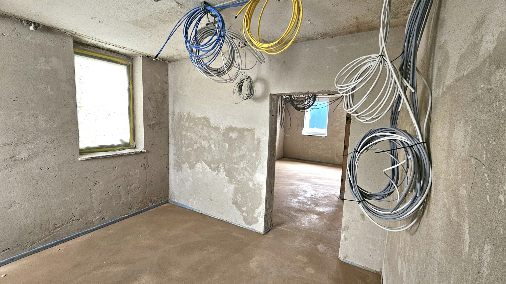 Blick in Räume mit neu verputzten Wänden. Von der Decke hängen Kabel in verschiedenen Farben.