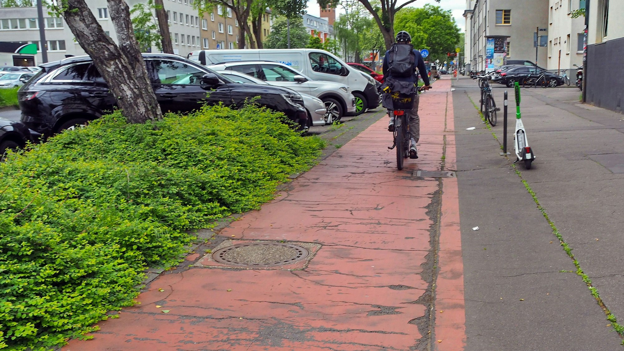 Ein rot markierter Radweg an einer großen Straße hat sehr viele Hubbel und Risse.