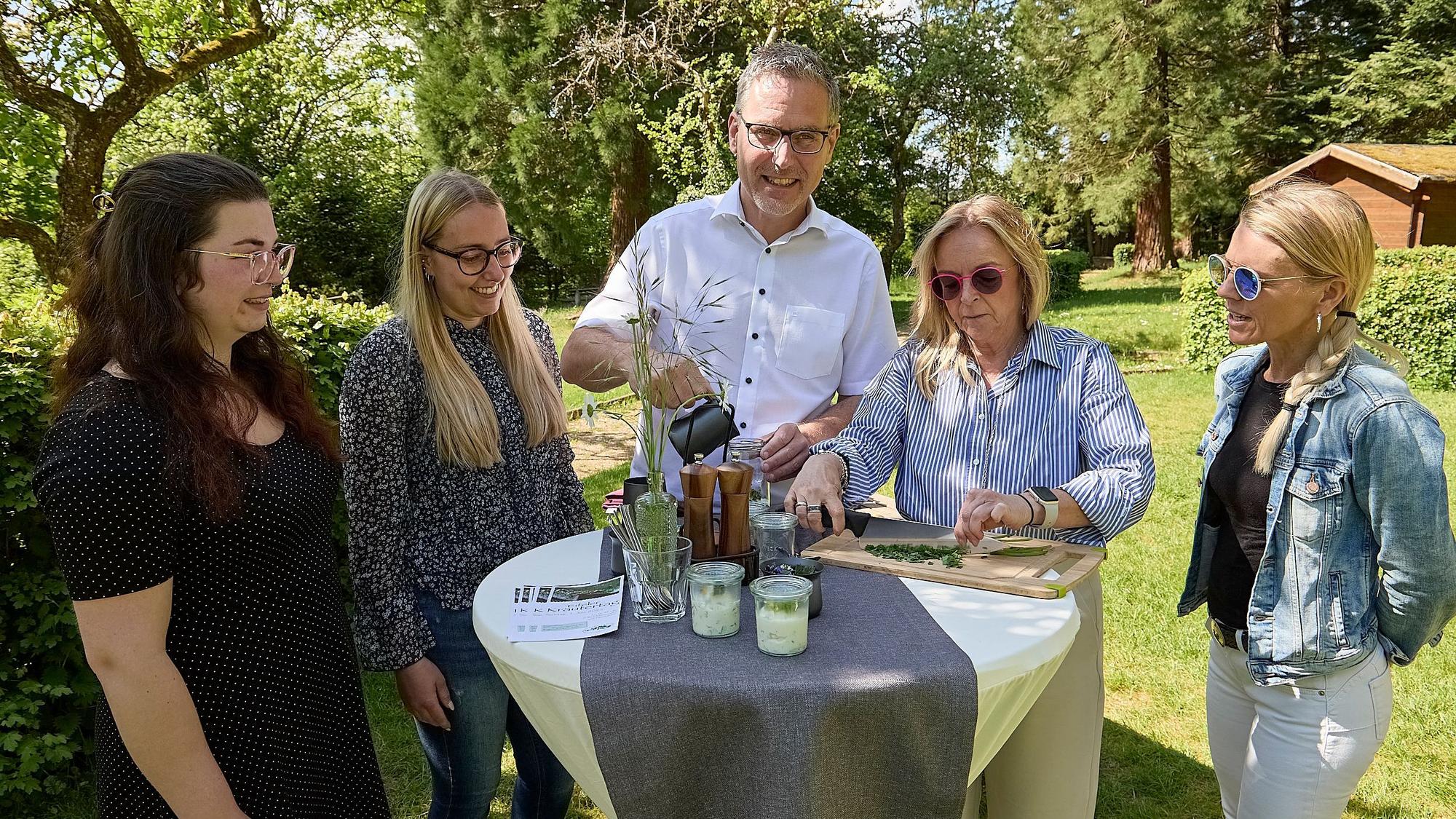 Ein Mann und vier Frauen stehen in einem Garten an einem Stehtisch.