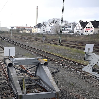 Ein Bahnhof. Der Bahnsteig ist menschenleer, im Vordergrund Bahngleise mit Endpollern.