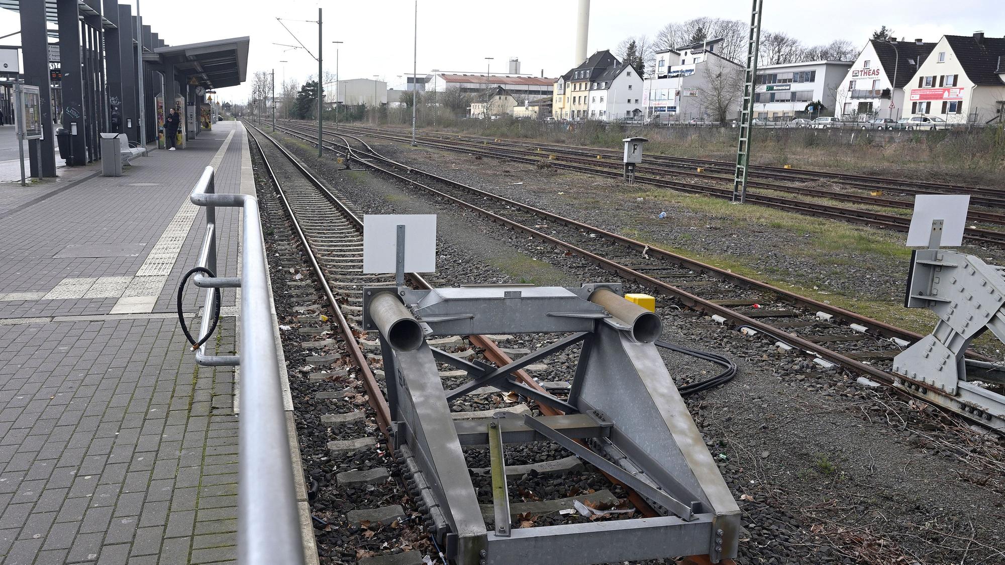 Ein Bahnhof. Der Bahnsteig ist menschenleer, im Vordergrund Bahngleise mit Endpollern.
