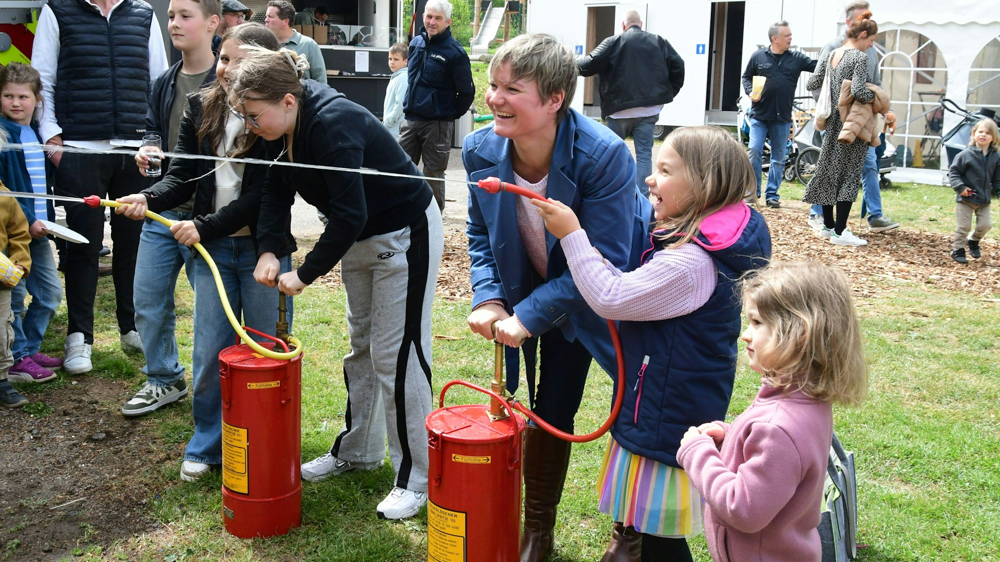 Kinder und Erwachsene stehen an Wasserspritzen und freuen sich, dass sie sie betätigen.