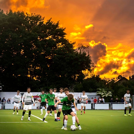 Das Bild zeigt eine Szene eines Fußballspiels. Im Hintergrund geht die Sonne unter.